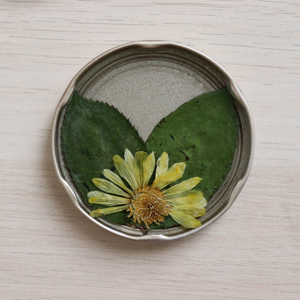 yellow flower on top of green leaves in a golden jar lid sealed in resin