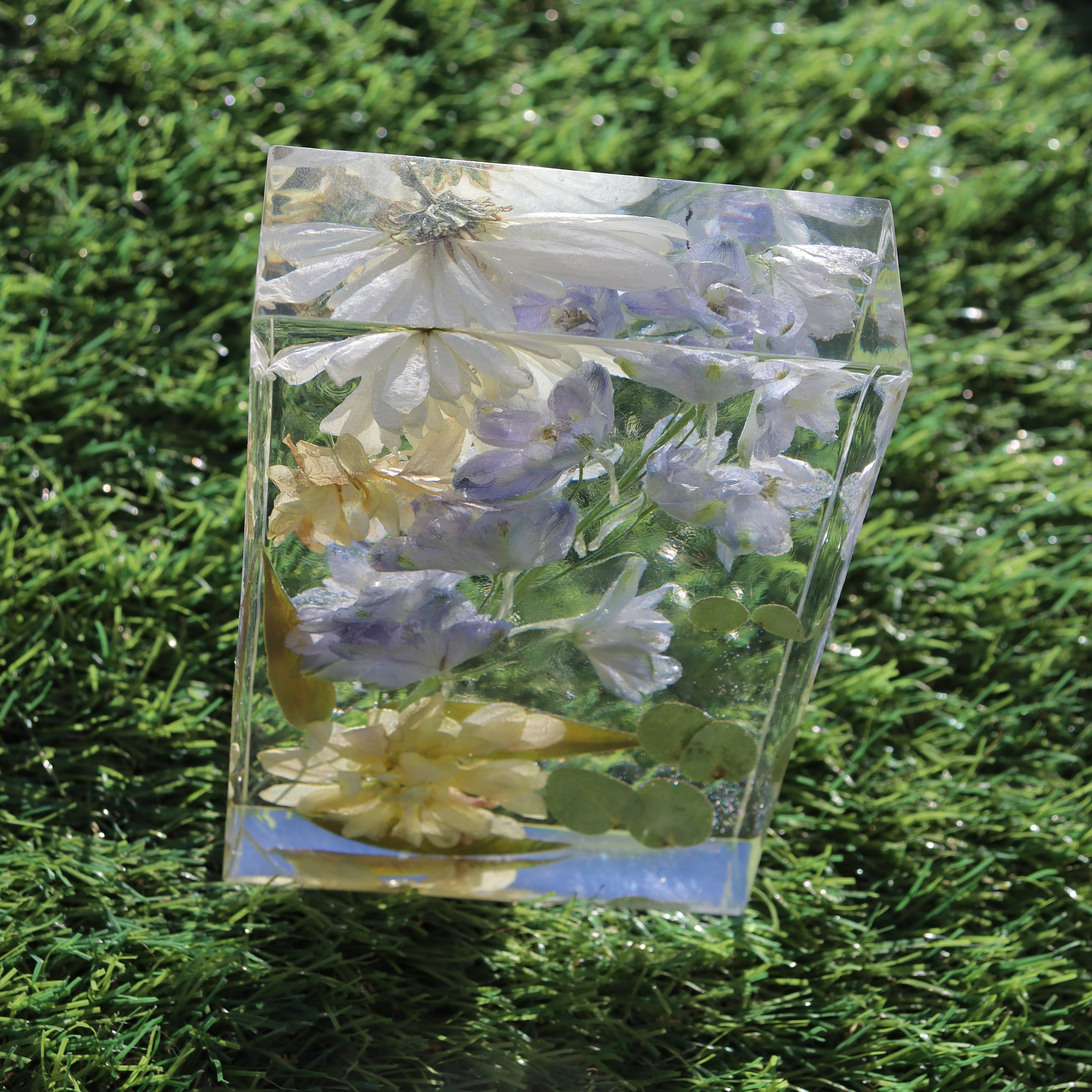 Close-up of dried florals suspended in a clear resin block on grass